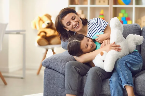 Mutlu anne ve kız kanepede dinleniyor ve evde oyuncaklarla oynuyor. — Stok fotoğraf