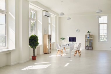 Geniş pencereli, beyaz masalı ve sandalyeli modern, parlak bir ofiste çalışma yeri.