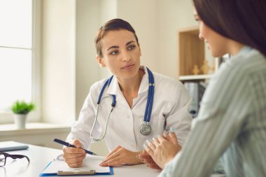 Klinikteki danışmanlık sırasında kadın hastaların şikayetlerini dinleyen olumlu bir doktor.