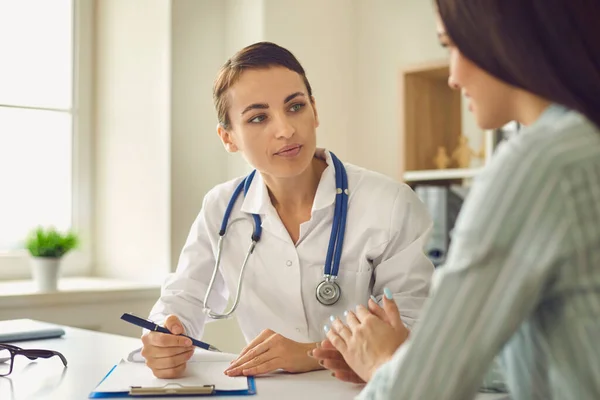 Terapeuta médico positivo sentado y escuchando las quejas de la paciente durante la consulta en la clínica médica —  Fotos de Stock