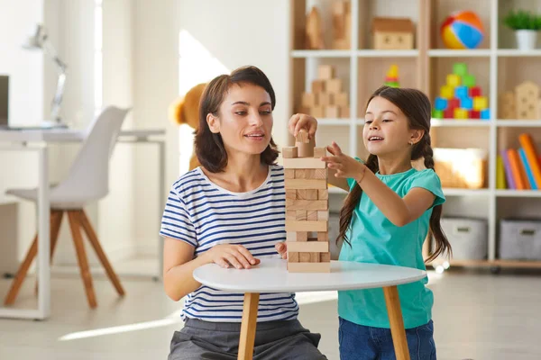 Mom and daughter playing and building tower out of wood blocks in cozy nursery at home — Stock Photo, Image