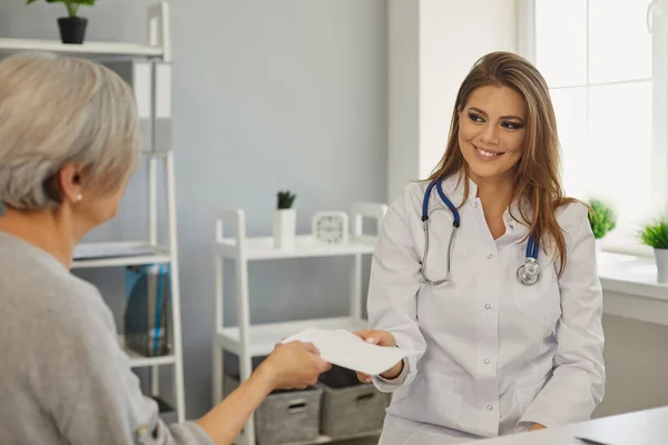 Doctor is giving a prescription to a patient while sitting at the workplace in a medical clinic office. — Stock Photo, Image