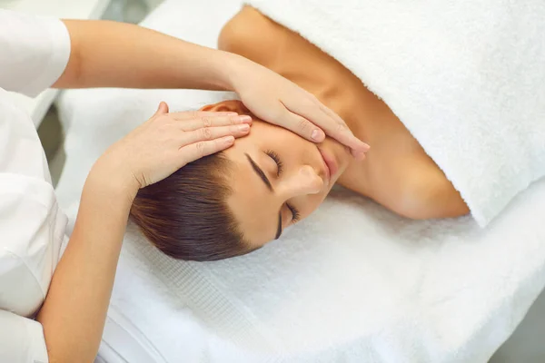 Jonge vrouw ligt op een bank en ontvangt een hoofd massage uit de handen van een masseur — Stockfoto
