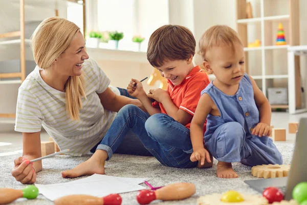 Ibu dan anak-anak yang bahagia duduk di lantai dan bermain bersama di rumah — Stok Foto