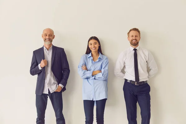 Three cheerful multi-aged office workers leaning against wall and looking at camera