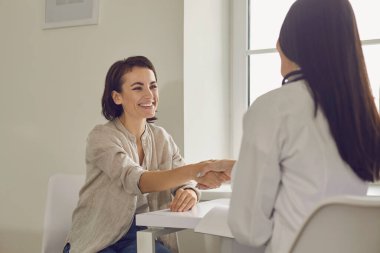 Tıbbi klinikte başarılı bir muayeneden sonra gülümseyen hasta el sıkışıyor.