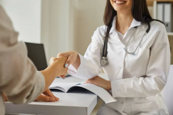 Freundliche Ärztin beruhigt ihre Patientin, die ihre Hand während eines Interviews im Krankenhaus sanft berührt — Stockfoto