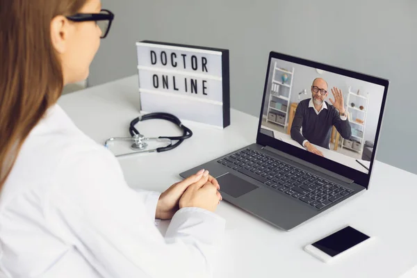 Donna medico seduto nello studio medico e guardando e salutando il suo paziente uomo online dal computer portatile — Foto Stock