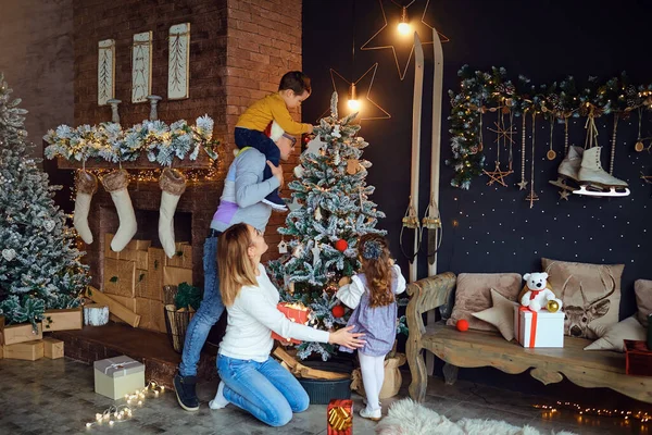 Madre e padre con bambini che decorano l'albero di Natale in camera — Foto Stock