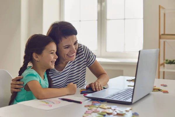 Счастливая мать и дочь сидят рядом с ноутбуком и ждут мультфильмы вместе — стоковое фото