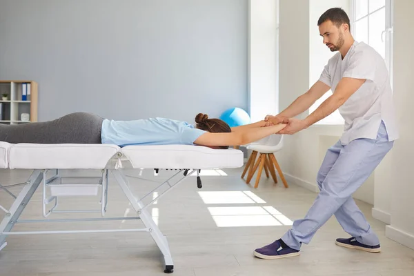 Muž chiropraktik nebo osteopat protahování ženy pacientky ruce a zpět během návštěvy na klinice manuální terapie — Stock fotografie