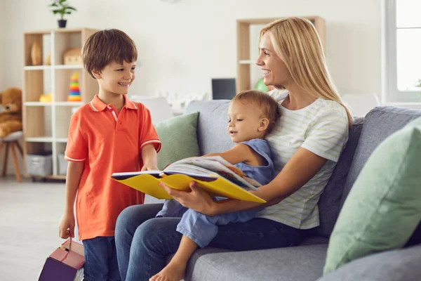 Ibu bahagia membaca buku dongeng untuk anak-anaknya duduk di sofa yang nyaman di rumah — Stok Foto