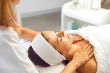 Kadın hasta, terapistin yüz ve omuzlarına elle rahatlatıcı masaj yaptırıyor.