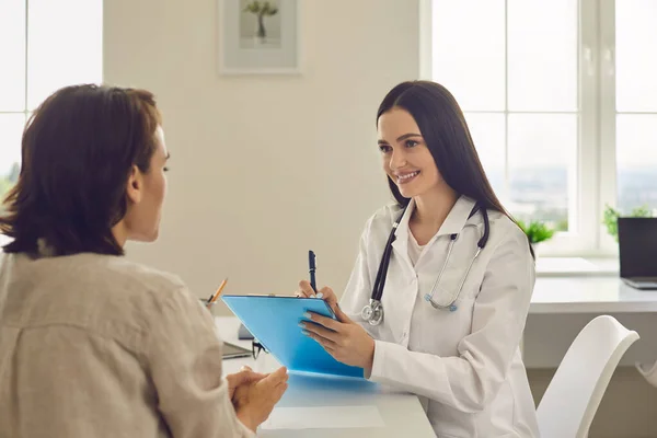 Jeune femme médecin souriante discute du diagnostic avec un patient dans un cabinet médical. — Photo