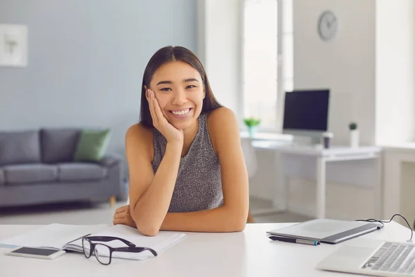 Veselý asijské dívka dívá na kameru sedí za stolem s notebookem a grafickým tabletem — Stock fotografie