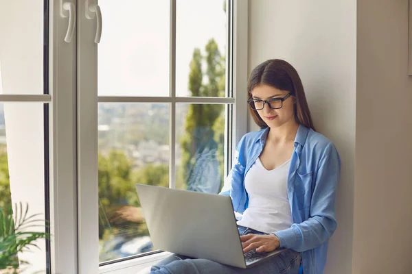Arbeiten von zu Hause aus. Junges Mädchen nutzt Laptop für Online-Videotelefonie oder Webkonferenz mit Chef, während sie auf der Fensterbank sitzt — Stockfoto