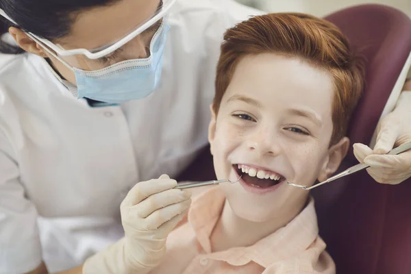 Menino ruivo de idade escolar feliz sendo examinado por dentista profissional do sexo feminino — Fotografia de Stock