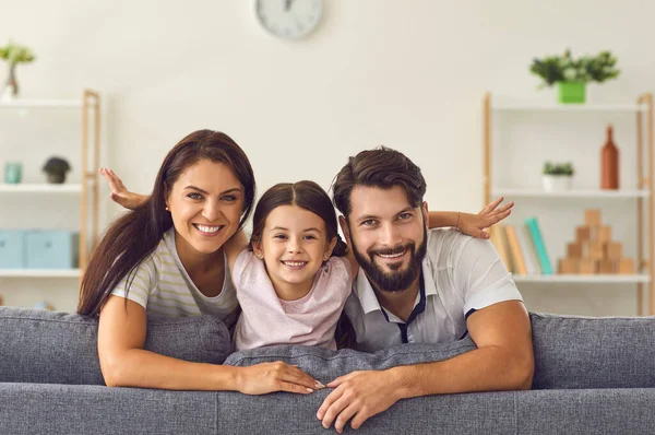 Szczęśliwa uśmiechnięta rodzina siedzi razem na kanapie i patrzy w kamerę w domu — Zdjęcie stockowe