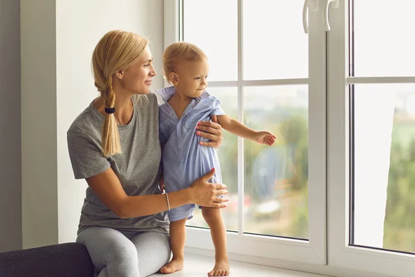 Ibu muda yang bahagia dan anak balita mengamati lingkungan dari jendela — Stok Foto