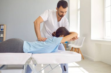 Modern sağlık merkezinde kadın hastaya kayropraktik sırt ayarlaması yapan profesyonel bir doktor.