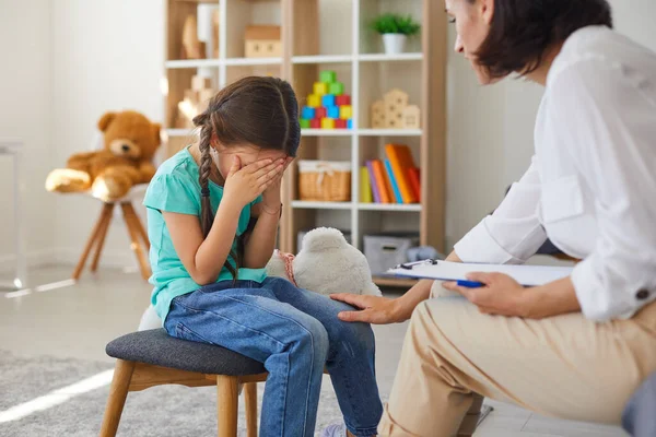 在看儿童心理医生的时候，小女孩坐在那里，用手捂住脸，哭泣 — 图库照片