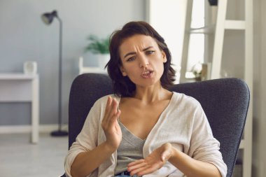 Genç bir kadın internet kamerasına bakıyor ve çevrimiçi toplantı sırasında elleriyle bir şey anlatıyor.