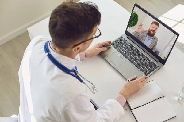 Uomo medico guardando lo schermo del computer portatile a salutarlo paziente uomo durante la consultazione online — Foto Stock