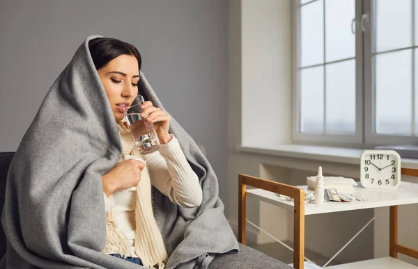 毛布の中の若い女性の側面図風邪をひいたとインフルエンザの薬を服用,飲料水. — ストック写真