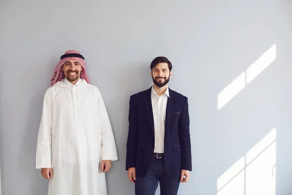 Арабские и европейские бизнесмены стоят и улыбаются на сером фоне. — стоковое фото
