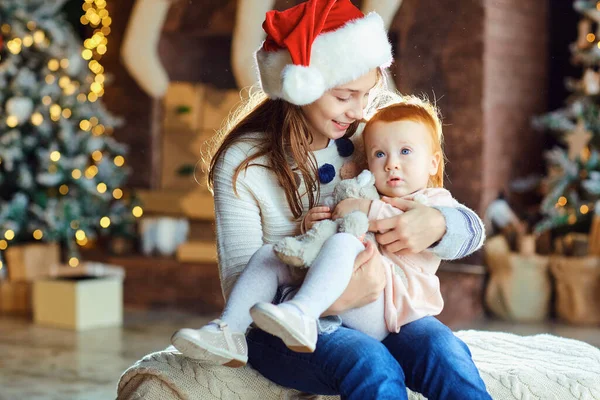 A girl in is holding a sister in her arms at Christmas. — Stock Photo, Image