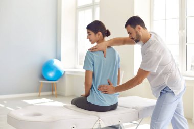Lisanslı osteopat modern hastane ofisinde genç kadın hastaları muayene ediyor.