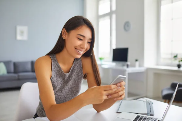 Smiling Asian blogger girl scrolling through social media news feed on mobile phone