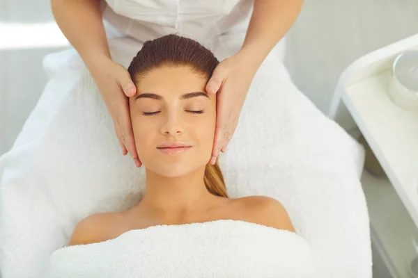 Красива жінка отримує масаж обличчя, що лежить з закритими очима на ліжку в салоні краси — стокове фото
