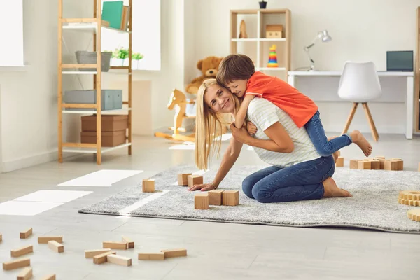 Preschool child embracing his young mommy from behind while having fun together at home — Stock Photo, Image