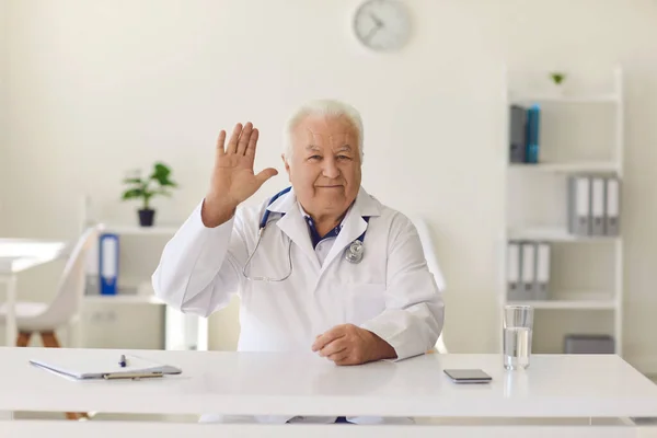 Friendly doctor waving hand welcoming clients in hospital office or on his medical video channel