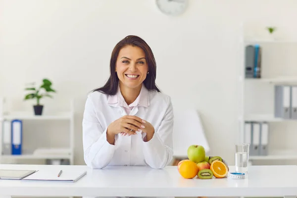 Glückliche Diätassistentin sitzt an ihrem Schreibtisch im Büro und lächelt in die Kamera — Stockfoto