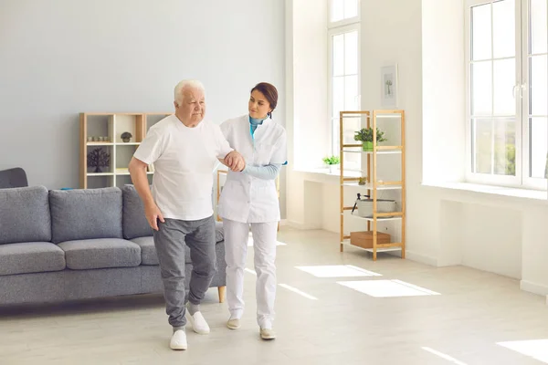 Zorgverlener helpt senior man om in het kantoor van moderne ziekenhuis of geriatrische revalidatiecentrum lopen — Stockfoto