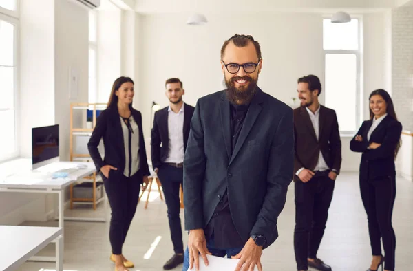 Joven empresario alegre con grupo de empleados sonriendo y mirando a la cámara —  Fotos de Stock