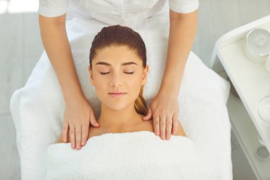 Güzellik salonunda gülümseyen bir kadın için yüz ve omuz masajı yapan kozmetik uzmanının elleri.