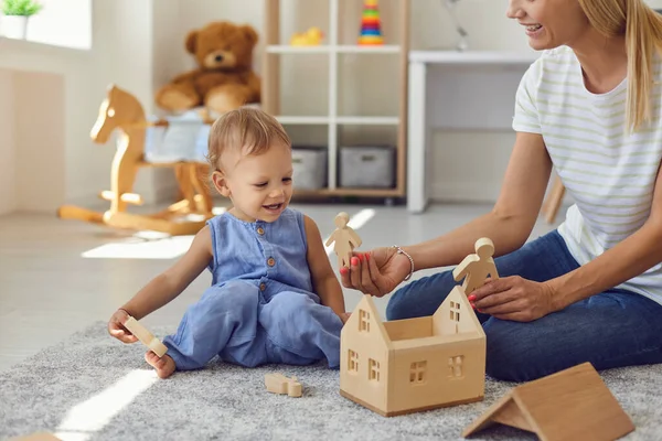 Joven niñera alegre y niño pequeño jugando con bloques de madera en la acogedora habitación del vivero —  Fotos de Stock
