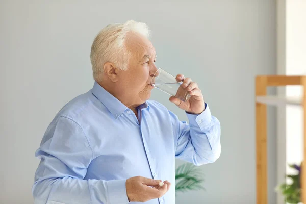 Witharige, mollige oudere man die voorgeschreven medicijnen inneemt met een glas water — Stockfoto