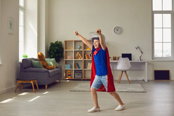 Opgewonden jongen in superheld cape en helm spelen thuis. Kind verkleed als stripfiguur plezier hebben binnen — Stockfoto