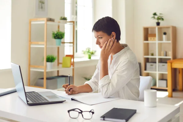 Mulher focada com notebook e caneta trabalhando em um escritório elegante brilhante em um laptop. — Fotografia de Stock