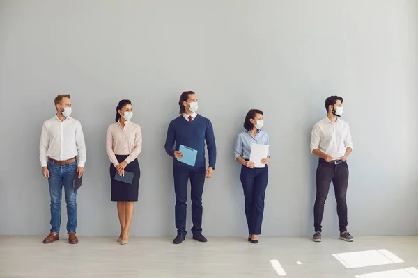 Job seekers in face masks waiting for job interview standing in corridor keeping safe distance