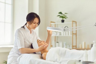 Cilt muayenesi sırasında gülümseyen dermatolog genç kadınların yüzüne bakıyor.