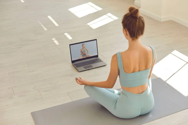 Тонка дівчина практикує тренування йоги під час онлайн-уроку на ноутбуці з віртуальним тренером на екрані — стокове фото
