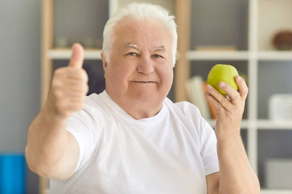 Gelukkig senior man kijken naar camera met verse groene appel en het geven van thumbs-up — Stockfoto