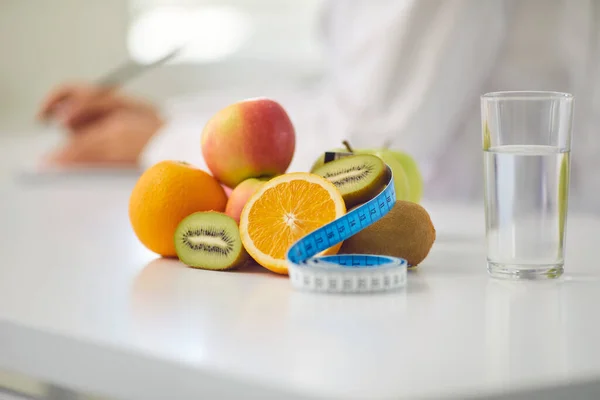 Local de trabalho de um nutricionista com frutas, um copo de água e uma fita métrica na mesa. — Fotografia de Stock