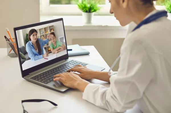 Doktor anne ve oğluyla yüksek ateşle iletişim kuruyor ve laptopta tavsiye veriyor.