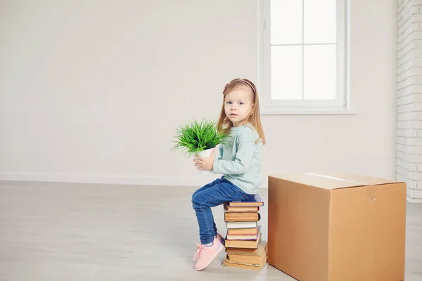 En flicka barn med en blomma sitter på lådorna för att flytta till ett nytt hus. — Stockfoto